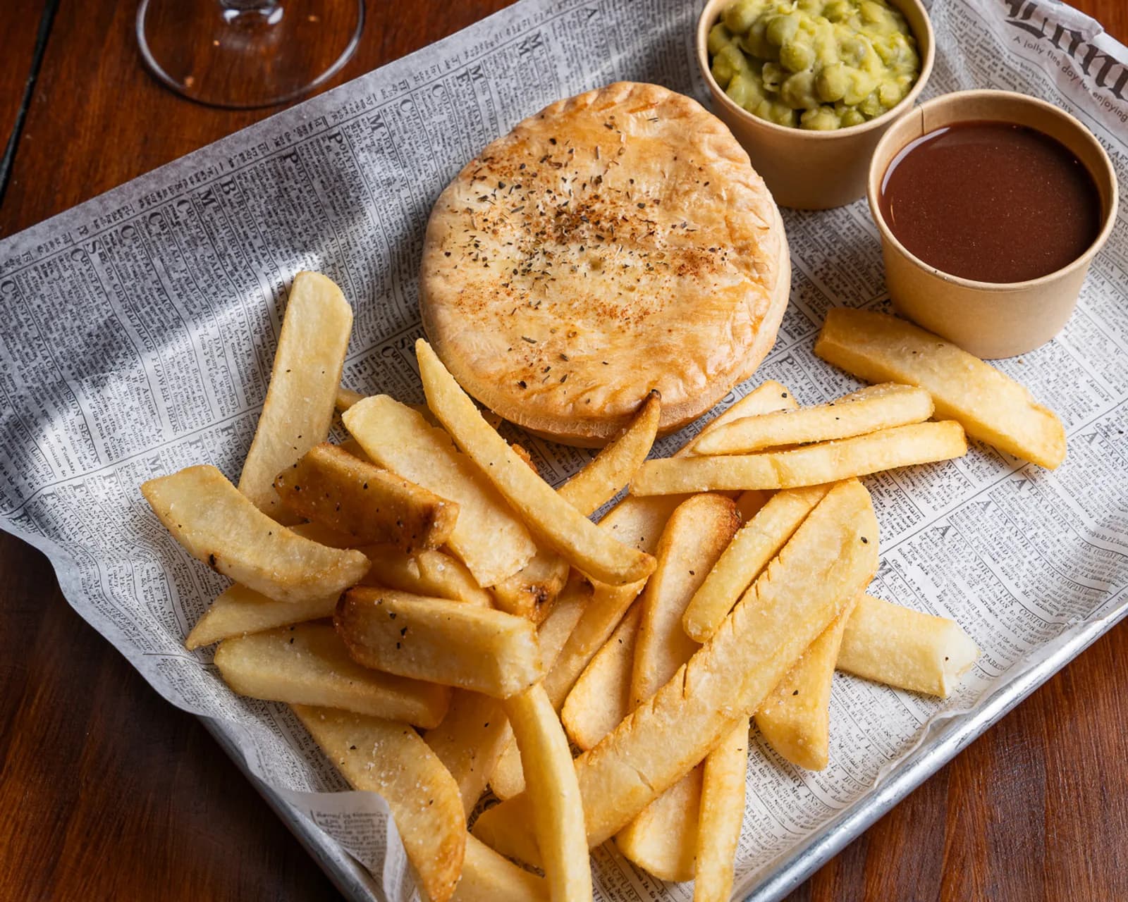Pie, chips, mushy peas and gravy on newspaper.
